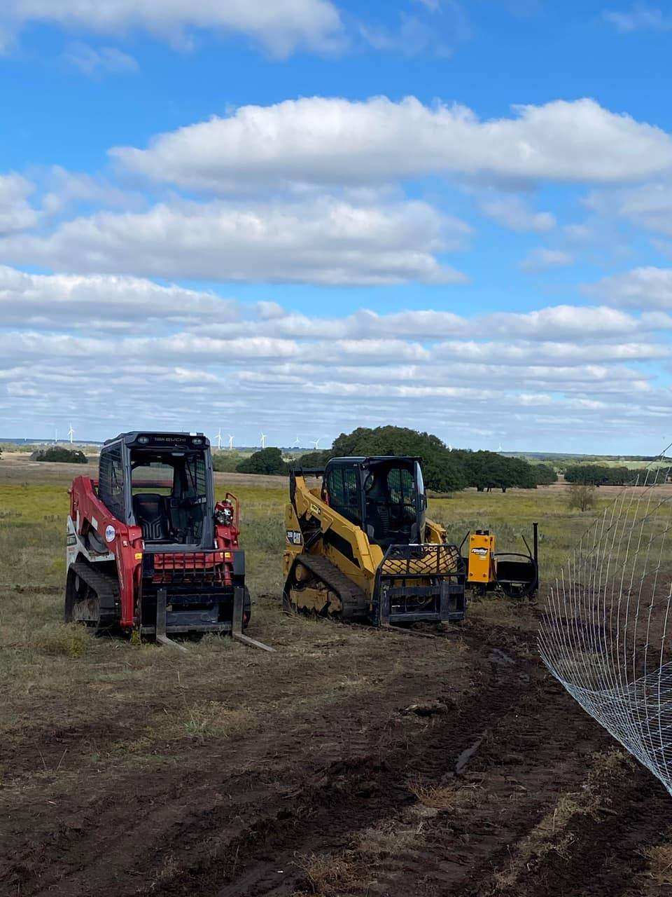 Linn's Fencing skid steer loaders staged with fencing attachments in a Central Texas pasture during a ranch fencing project.